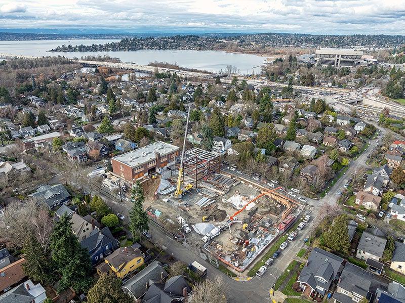 aerial view of a construction site surrounded by streets and houses with a lake and a stadium in the distance