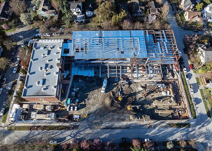 aerial view of a construction site with a brick building to the right and a new building being constructed at a right angle attached to it in the upper part of the photo. dirt and construction equipment are in the remaining space