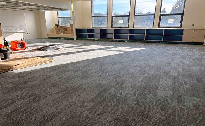 a large room with shelves under the windows has carpet being installed